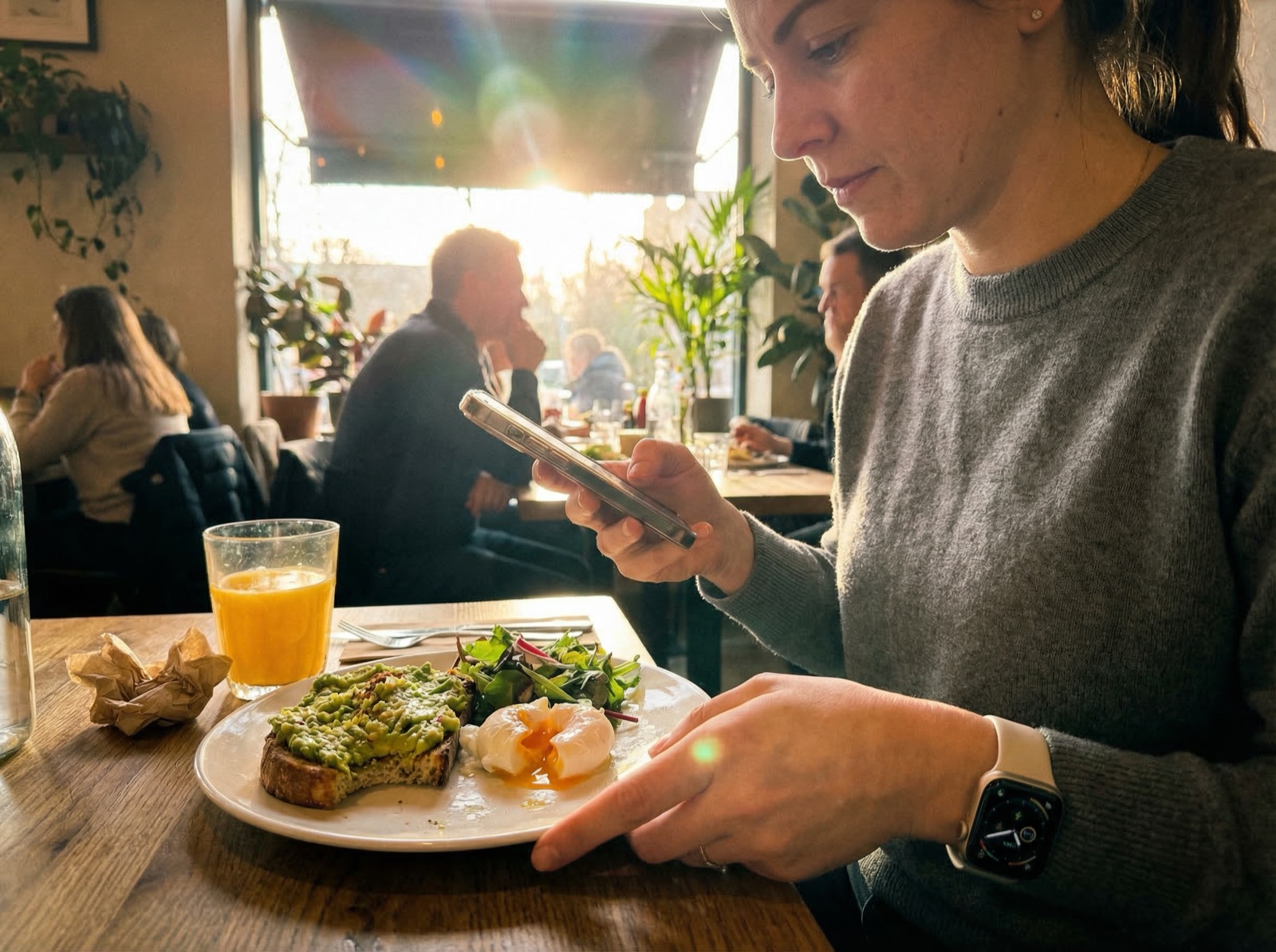 Woman logging her brunch in a food journal app on her phone at a bright cafe